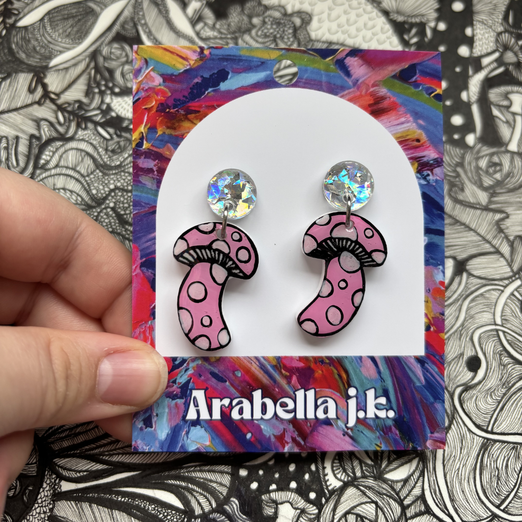 Pink mushroom-shaped earrings on a colorful 'Arabella j.k.