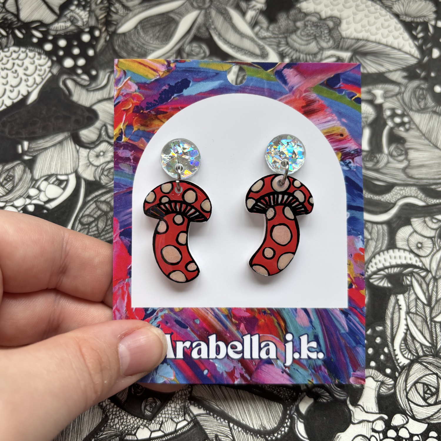 Red mushroom-shaped earrings on a colorful card with 'Arabella J.K.